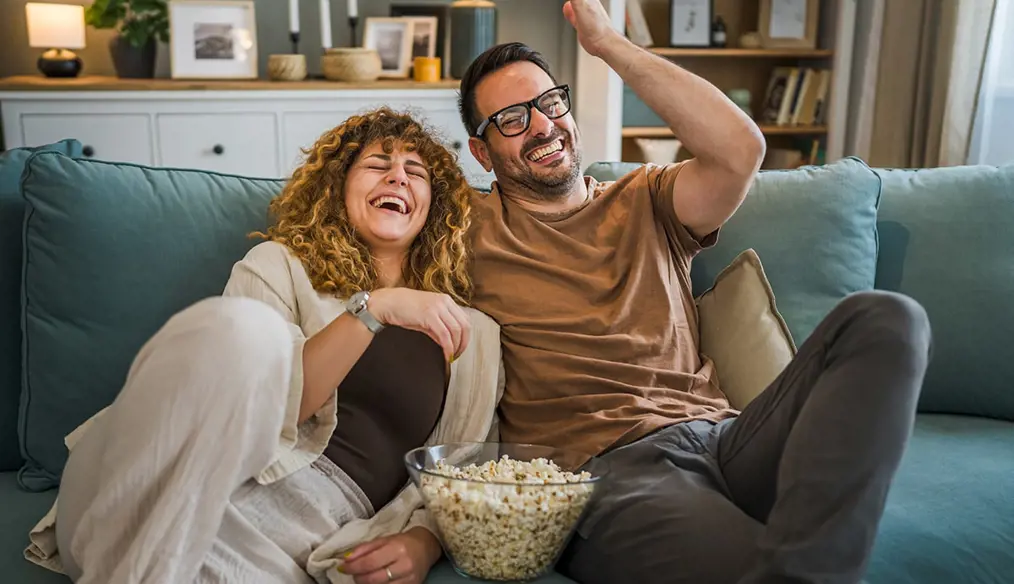 laughing couple with bowl of popcorn on the sofa