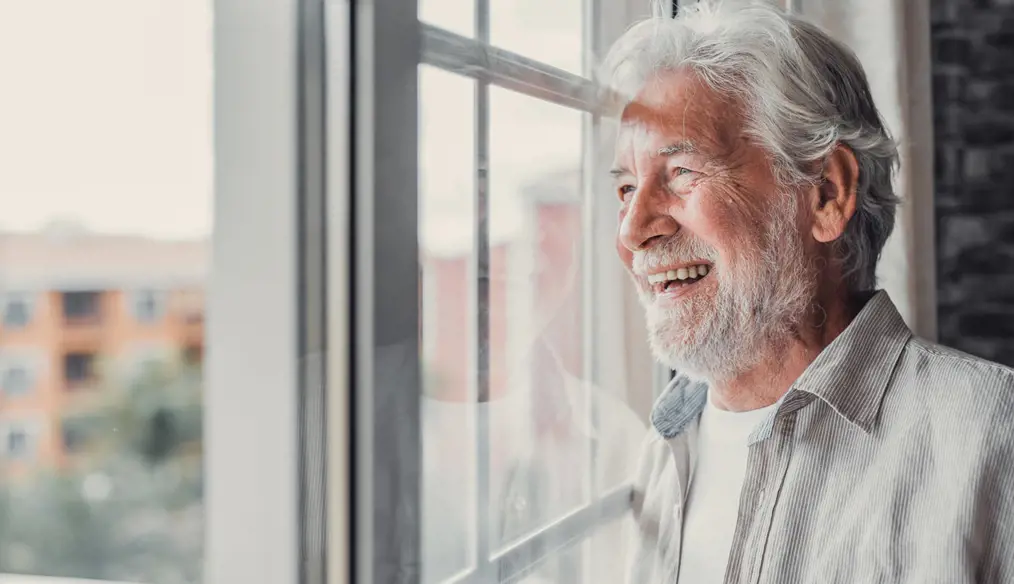 Elderly man looking out the window and smiling